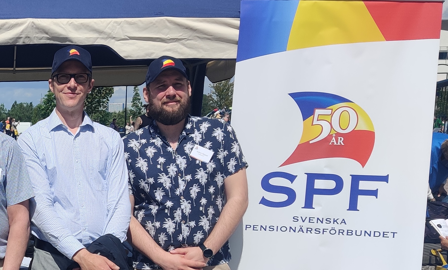Andreas och Robert står i solskenet med kepsar på, till höger SPFs logo