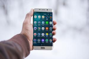 En hand sträcker fram en smarttelefon med skärmen full av appar