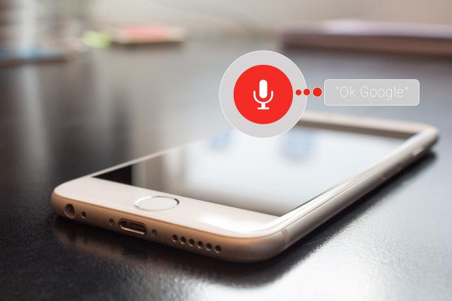 En telefon som ligger på bordet med en röd mikrofon ikon ovanför. Bredvid ikonen står det ok google